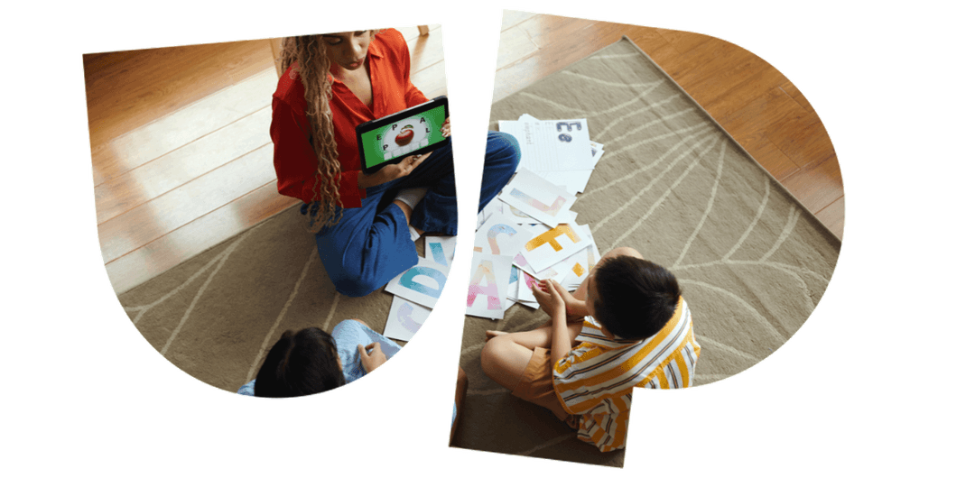 Two people sitting on a carpet, viewing a tablet and colorful papers spread around them.