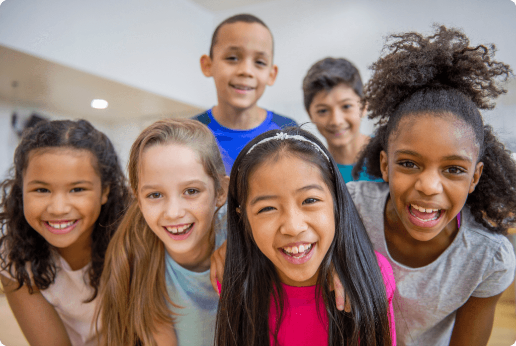 Six smiling children pose closely together in a bright room, conveying joy and friendship.